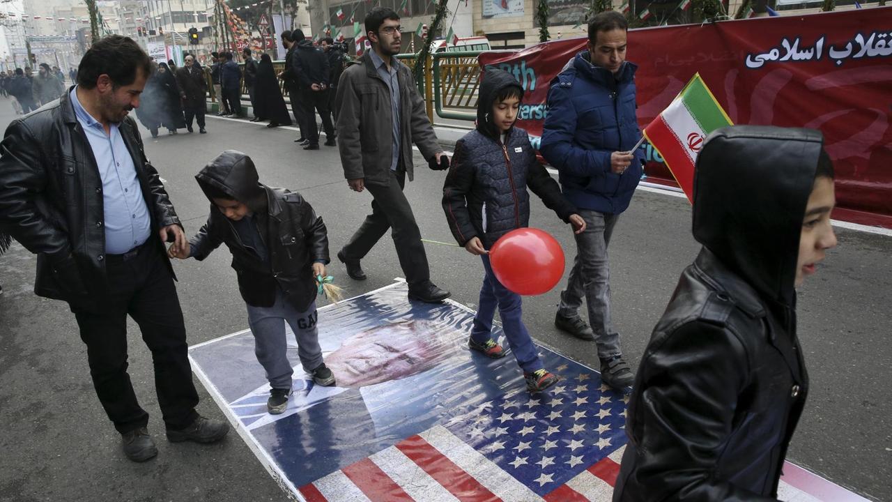 Menschen laufen in Teheran (Iran) bei der jährlichen Kundgebung anlässlich des Jahrestags der islamischen Revolution über eine am Boden angebrachte US-Flagge mit einem Porträt von US-Präsident Trump-