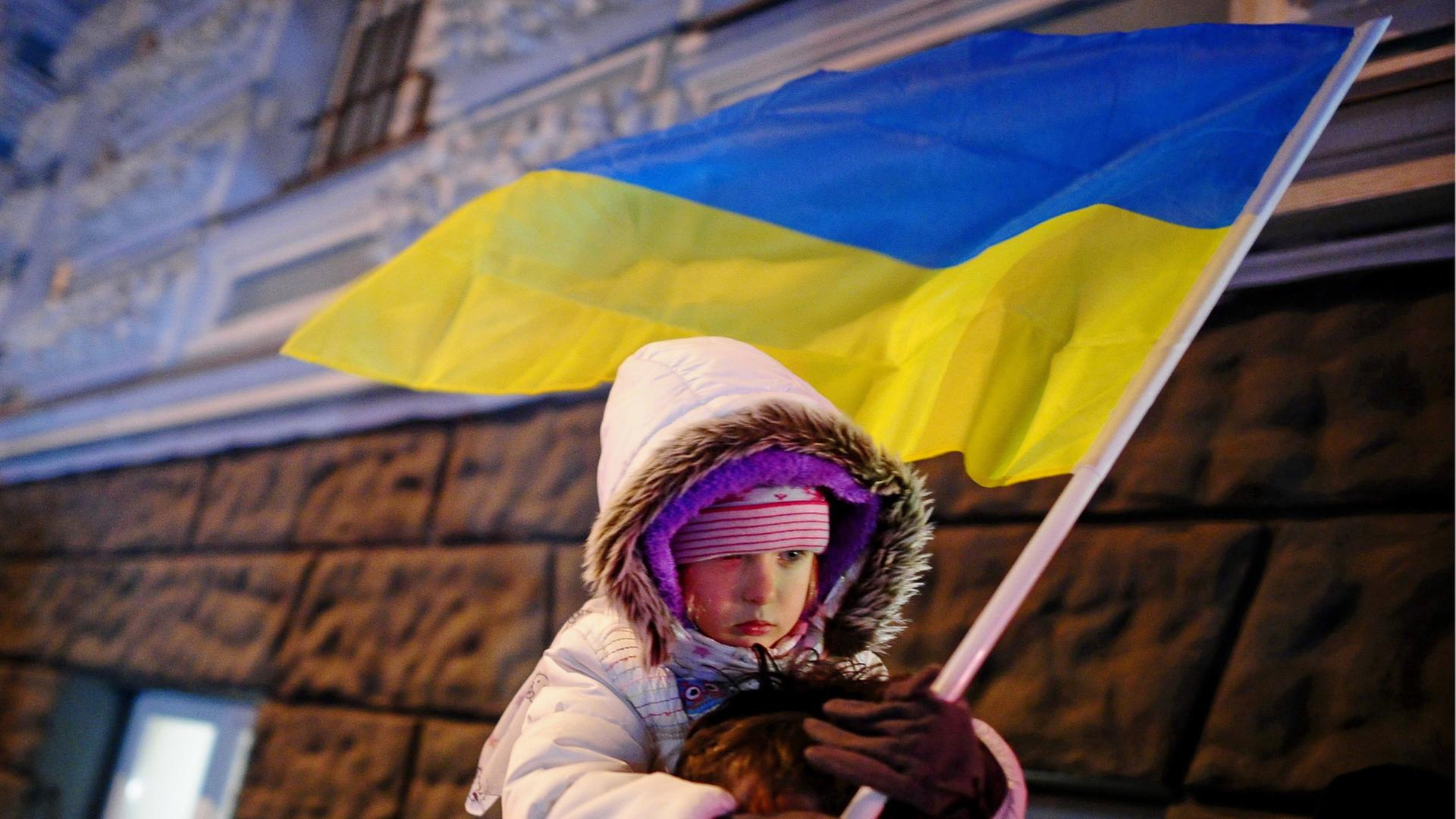 Vater trägt sein Kind, das in der Hand eine ukrainische Flagge hält, bei Protesten in Kiew am 30.11.2013