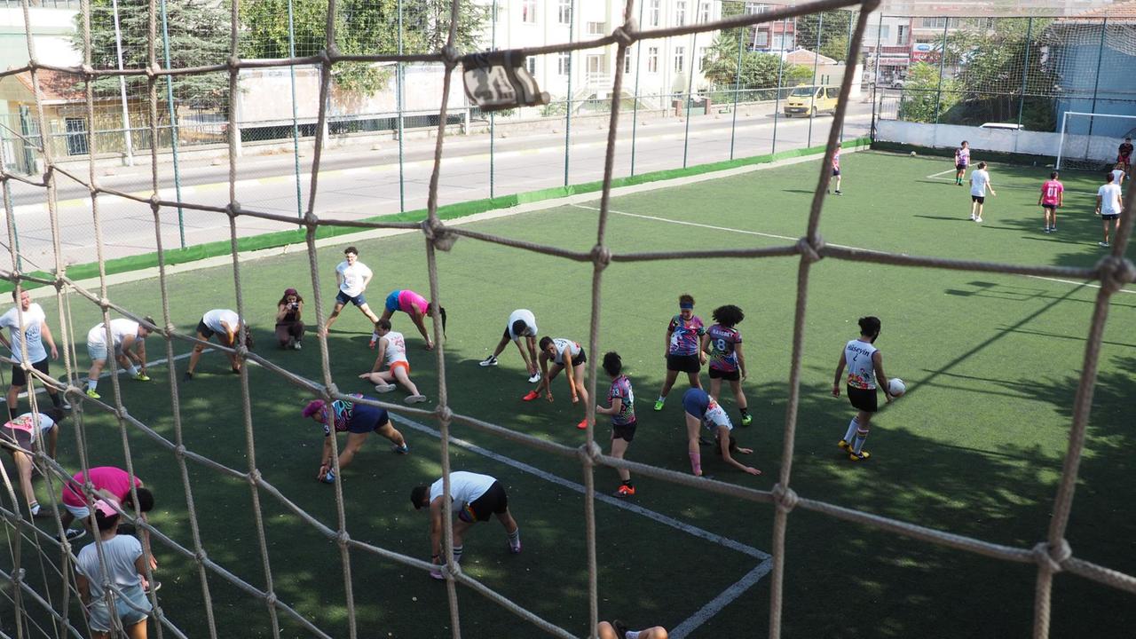 Blick durch ein Netz von oben herunter auf ein Fußballfeld mit Spieler:innen.