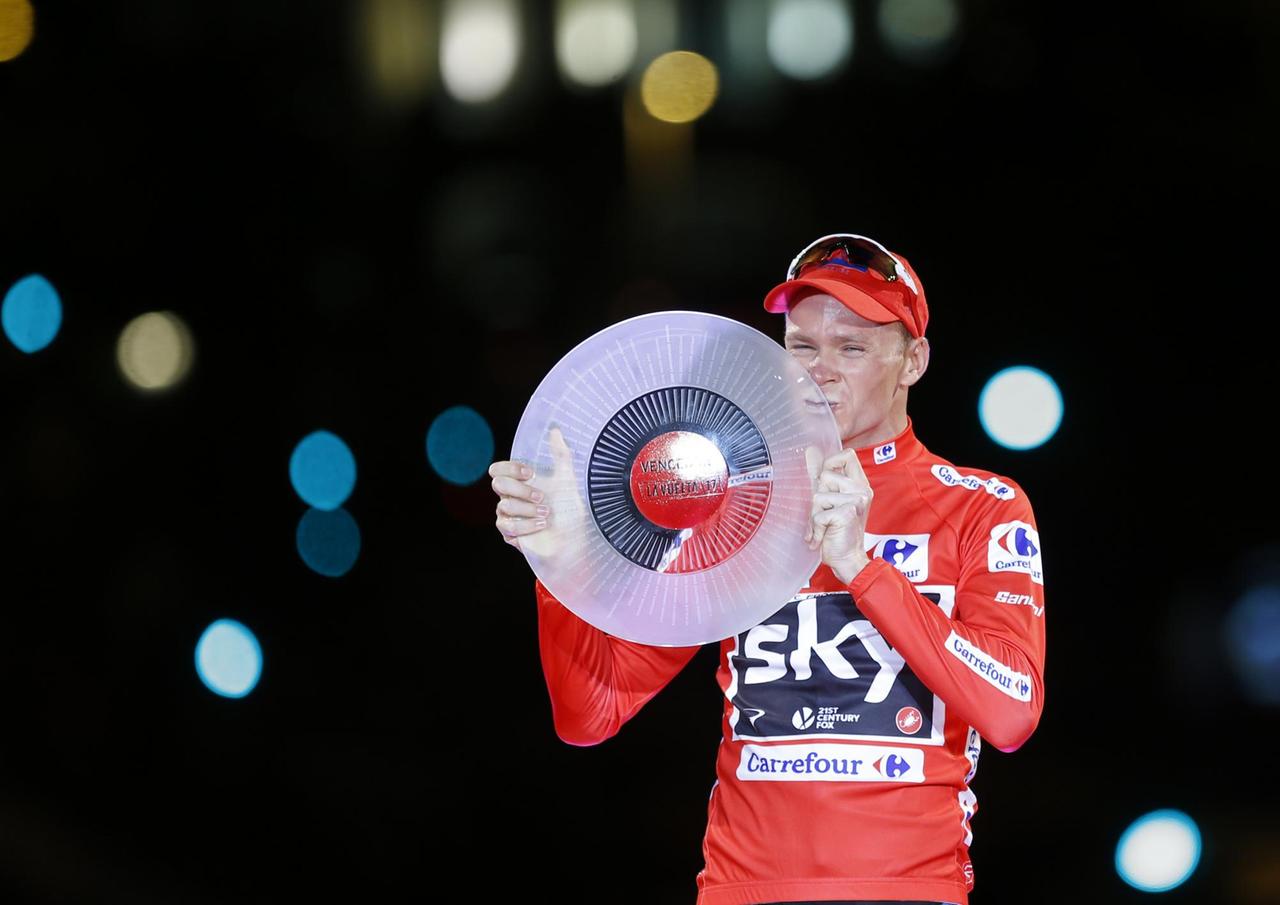 Froome im roten Trikot und mit roter Mütze küsst seine Trophäe: Eine milchglasige Scheibe. Der Hintergrund ist dunkel bis auf einige Farbreflexe. Froome im roten Trikot und mit roter Mütze küsst seine Trophäe: Eine milchglasige Scheibe. Der Hintergrund ist dunkel bis auf einige Farbreflexe.