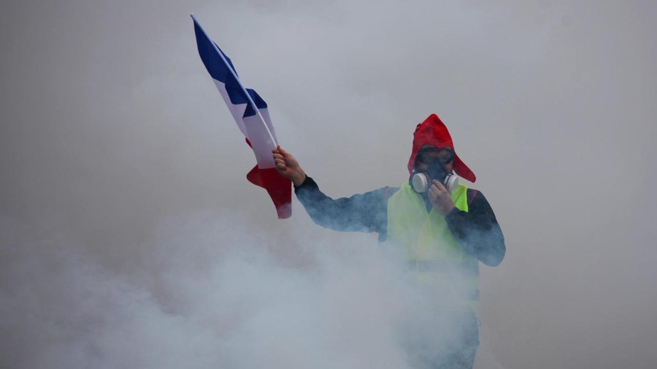 Ein Demonstrant der "Gelbwesten" mit einer französischen Flagge inmitten von Tränengas in Paris Ein Demonstrant der "Gelbwesten" mit einer französischen Flagge inmitten von Tränengas in Paris