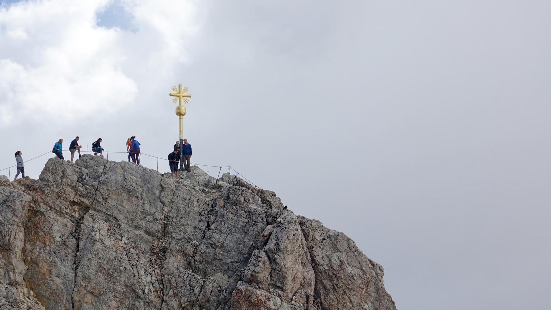 Bergsteiger stehen Schlange vor einem goldenen Gipfelkreuz Bergsteiger stehen Schlange vor einem goldenen Gipfelkreuz