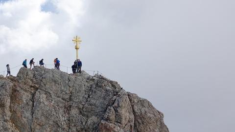Bergsteiger stehen Schlange vor einem goldenen Gipfelkreuz