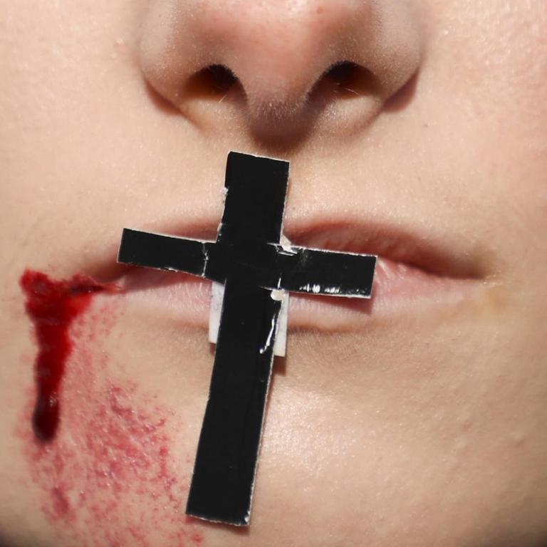 Auf einem Mund klebt ein Kreuz. Im Gesicht sind aufgemalte Wunden zu sehen. Das Bild ist ein Symbolbild für die Folgen von Homophobie in Polen.