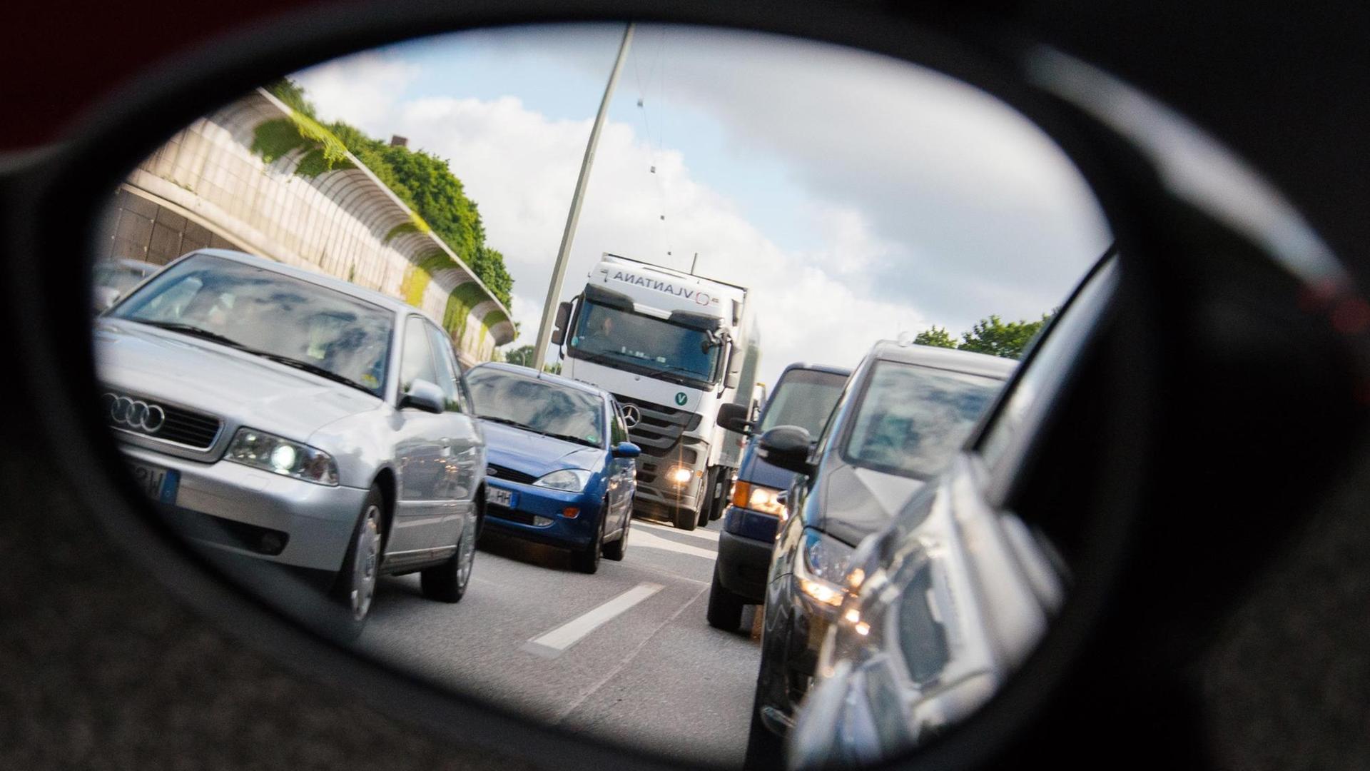 Autos und Lastwagen stehen am 20.06.2015 in Hamburg auf der Autobahn 7 bei Stellingen im Stau und sind dabei durch einen Rückspiegel zu sehen.