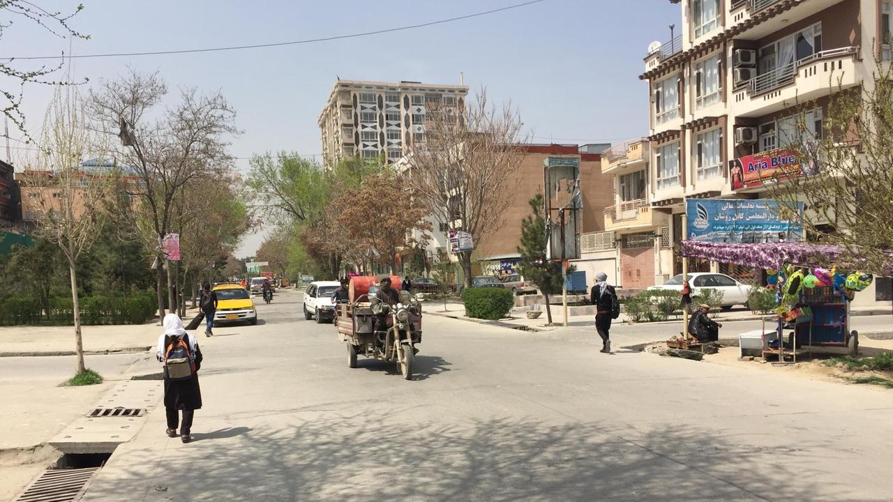 Auf einer von Wohnblocks gesäumten Straße in Kabul fahren vereinzelte Autos, am Rand laufen Menschen. Auf einer von Wohnblocks gesäumten Straße in Kabul fahren vereinzelte Autos, am Rand laufen Menschen.