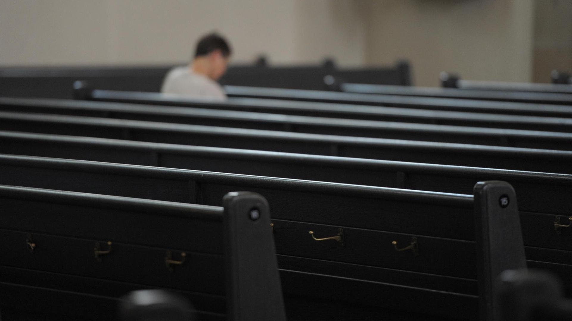 Ein einzelner Mensch sitzt in den ansonsten leeren Kirchenbänken. Ein einzelner Mensch sitzt in den ansonsten leeren Kirchenbänken.