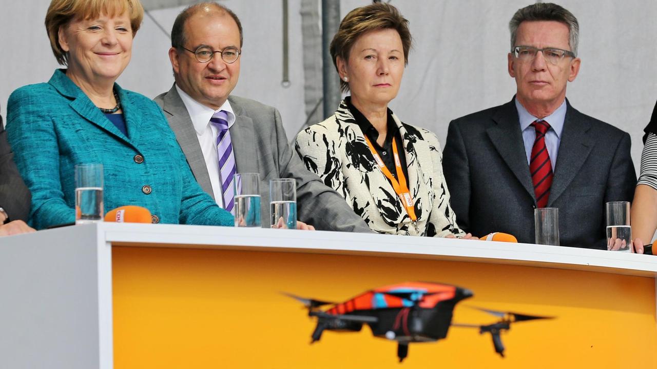 Bundeskanzlerin Angela Merkel (CDU, links im Bild) beobachtet mit dem damaligen Bundesverteidigungminister Thomas de Maizière (ganz rechts) die Landung einer Spielzeugdrohne während einer Wahlkampftour 2013 in Dresden