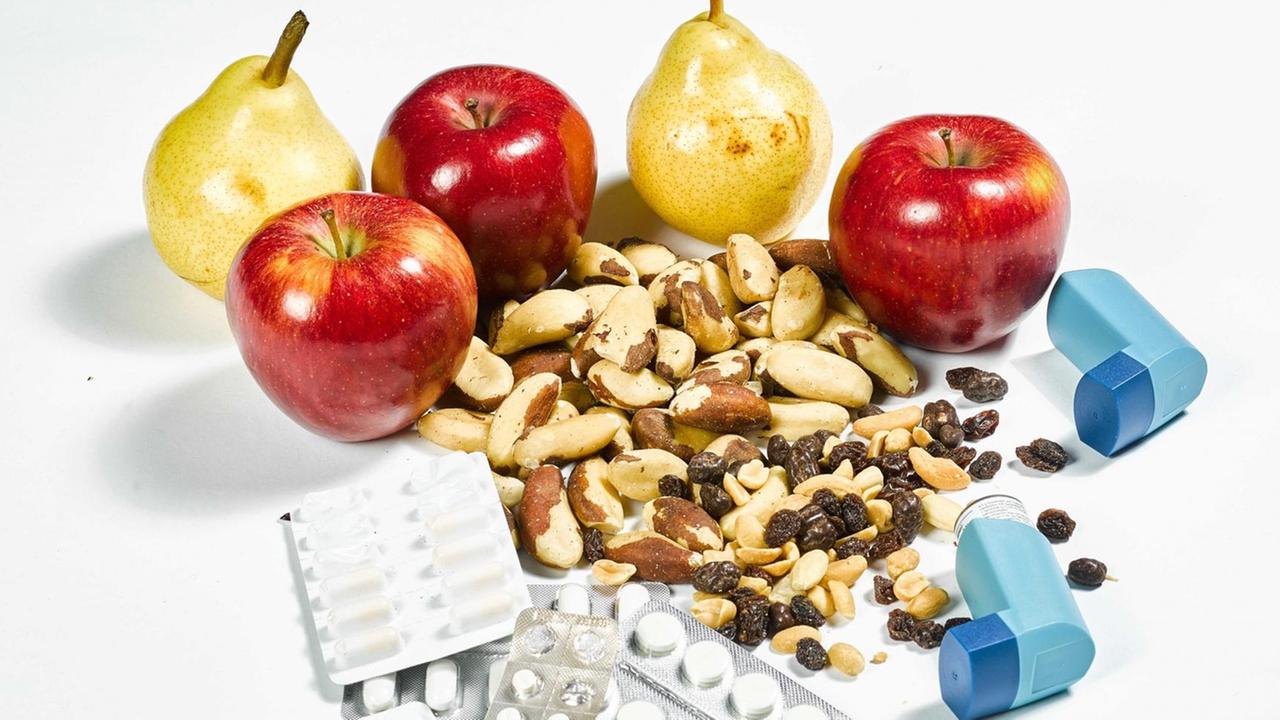 Äpfel, Birnen, Nüsse, Tabletten und Inhalatoren liegen auf einer weißen Fläche.