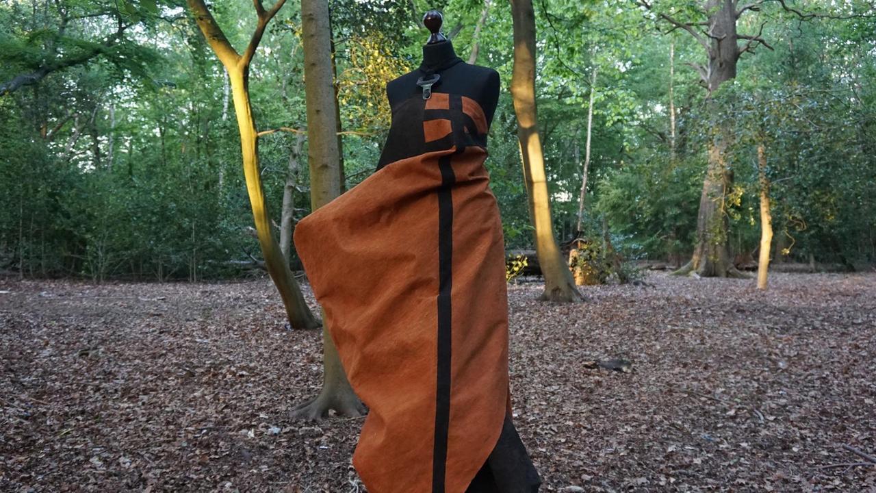 Ein schwarz-rotes Kleid ist inmitten einer Waldlichtung auf einen Kleiderständer drapiert. Ein schwarz-rotes Kleid ist inmitten einer Waldlichtung auf einen Kleiderständer drapiert.