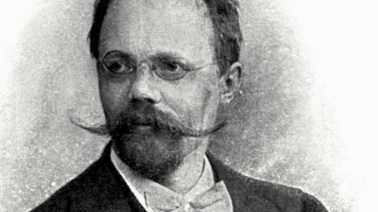Ein Bild eines Mannes mittleren Alters mit runder Brille und großen, weit schwingendem Schnurrbart. Ein Bild eines Mannes mittleren Alters mit runder Brille und großen, weit schwingendem Schnurrbart.
