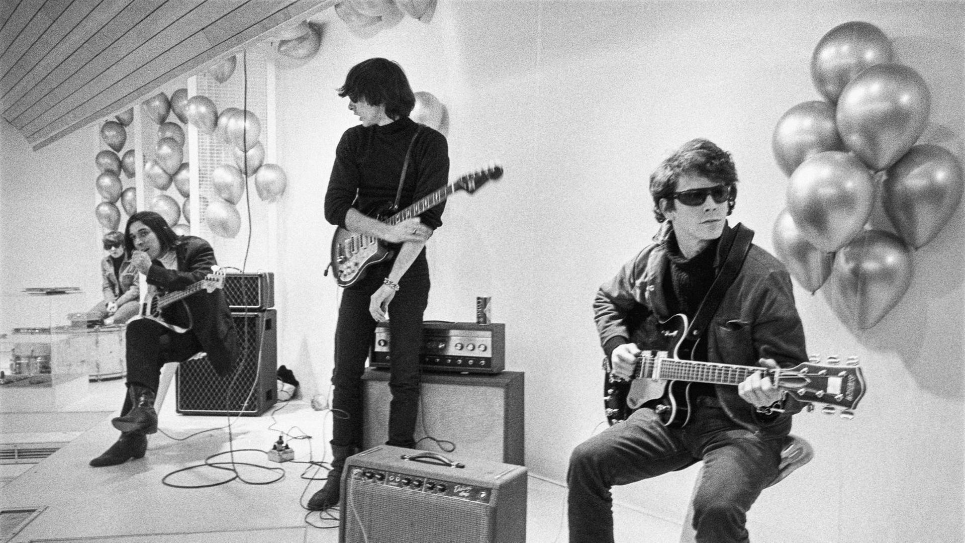 Moe Tucker, John Cale, Sterling Morrison und Lou Reed sitzen beziehungsweise stehen in einem weißen Raum. Sie tragen schwarze Kleidung, Lou Reed rechts eine Sonnenbrille. Sie haben ihre Instrumente und Verstärker bei sich. Moe Tucker, John Cale, Sterling Morrison und Lou Reed sitzen beziehungsweise stehen in einem weißen Raum. Sie tragen schwarze Kleidung, Lou Reed rechts eine Sonnenbrille. Sie haben ihre Instrumente und Verstärker bei sich.