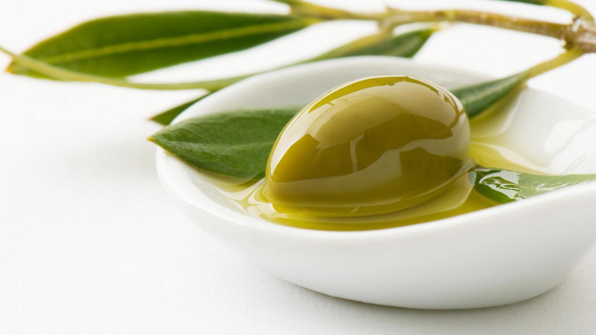 Eine Olive liegt in einer Schale mit Olivenöl Eine Olive liegt in einer Schale mit Olivenöl