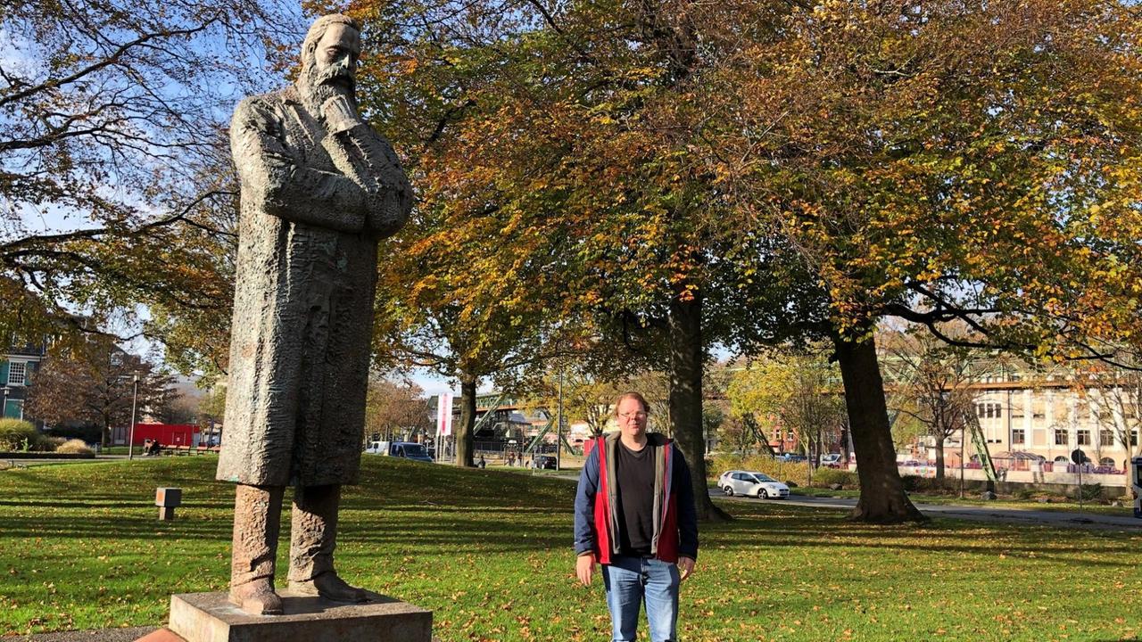 Christoph Grothe neben dem Friedrich-Engels-Denkmal in Wuppertal in einem Park.
