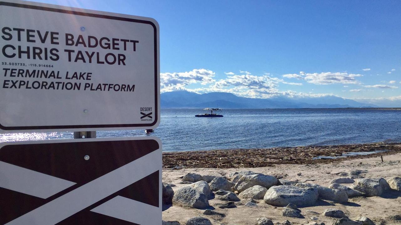 "Steve Badgett, Chris Taylor: Terminal Lake Exploration Platform" steht auf einem Schild am Strand von Salton Sea "Steve Badgett, Chris Taylor: Terminal Lake Exploration Platform" steht auf einem Schild am Strand von Salton Sea