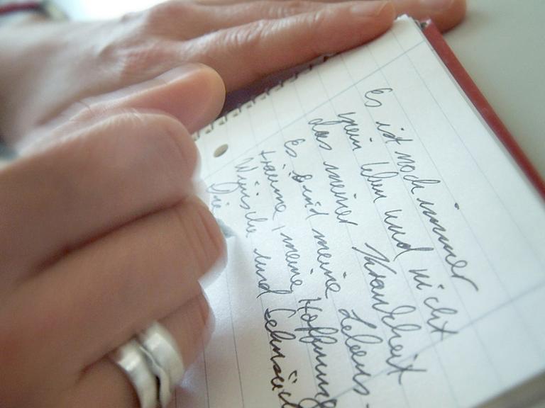 Eine Frau schreibt ihre Gedanken und Gefühle in einen Schreibblock.