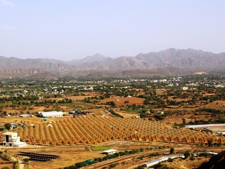 In einer Ebene von Rajasthan stehen zahlreiche Parabolschüsseln des solarthermischen Kraftwerks "India One". Im Hintergrund sind kahle Berge zu sehen. In einer Ebene von Rajasthan stehen zahlreiche Parabolschüsseln des solarthermischen Kraftwerks "India One". Im Hintergrund sind kahle Berge zu sehen.