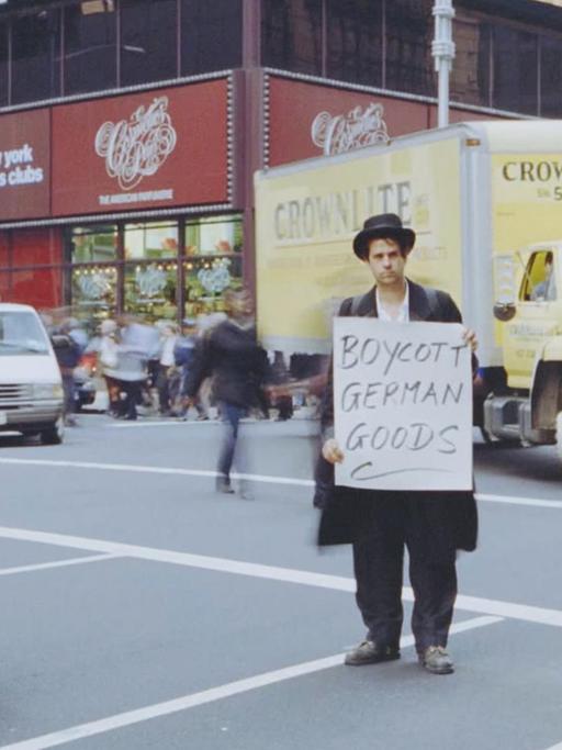 Szene aus dem Dokumentarfilm "Schlingensief - in das Schweigen hineinschreien": Christoph Schlingensief steht, als traditioneller Jude verkleidet, auf einer Straße in New York. Er hält ein Schild mit dem Aufdruck "Boycott German Goods".