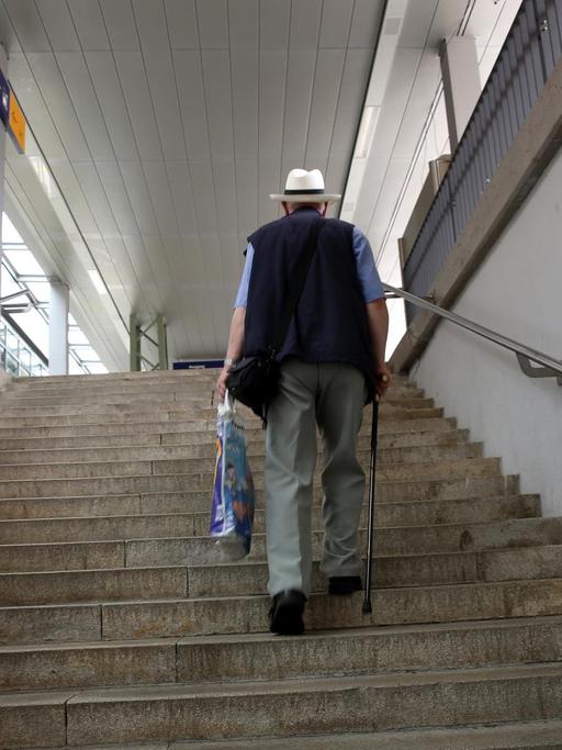 Ein älterer Herr mit Gehstock trägt eine Plastiktüte und steigt eine Treppe hoch.