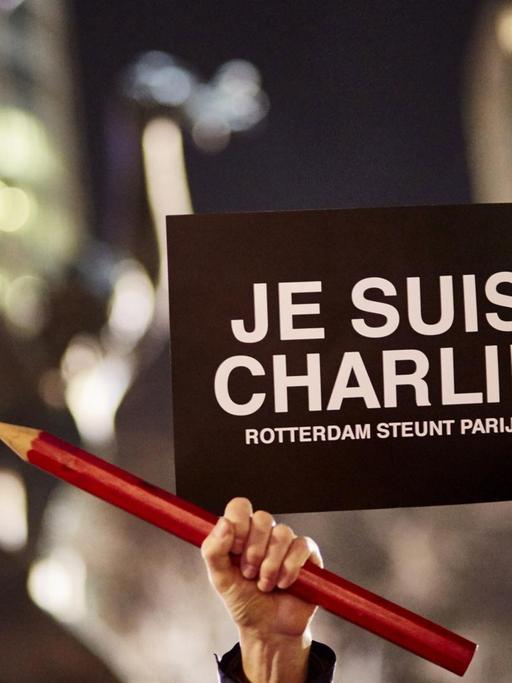 Weltweit wurde an die ermodeten Satiriker von "Charlie Hebdo" erinnert. In Rotterdam hält jemand einen Stift und ein Transparent in die Luft.