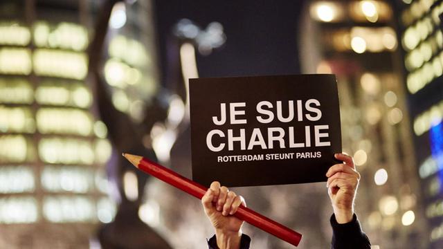 Weltweit wurde an die ermodeten Satiriker von "Charlie Hebdo" erinnert. In Rotterdam hält jemand einen Stift und ein Transparent in die Luft.