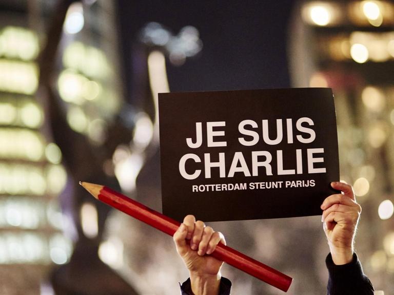 Weltweit wurde an die ermodeten Satiriker von "Charlie Hebdo" erinnert. In Rotterdam hält jemand einen Stift und ein Transparent in die Luft.