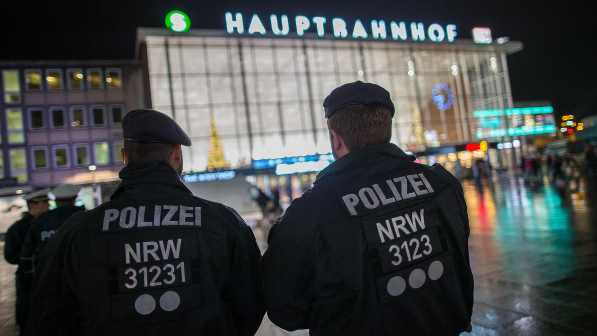 Polizisten stehen am Abend mit dem Rücken zur Kamera vor dem Kölner Hauptbahnhof. Polizisten stehen am Abend mit dem Rücken zur Kamera vor dem Kölner Hauptbahnhof.