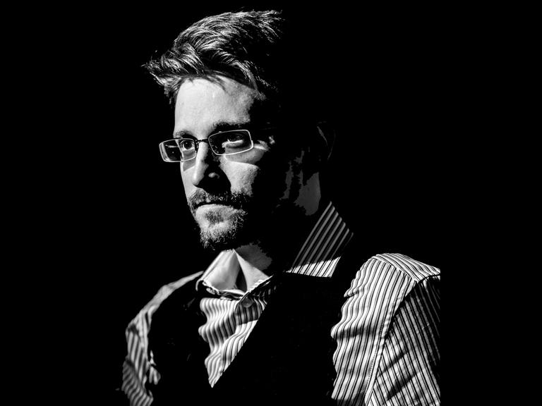 Edward Snowden blickt im halbdunkel und im Halbprofil stehend links am Betrachter vorbei.