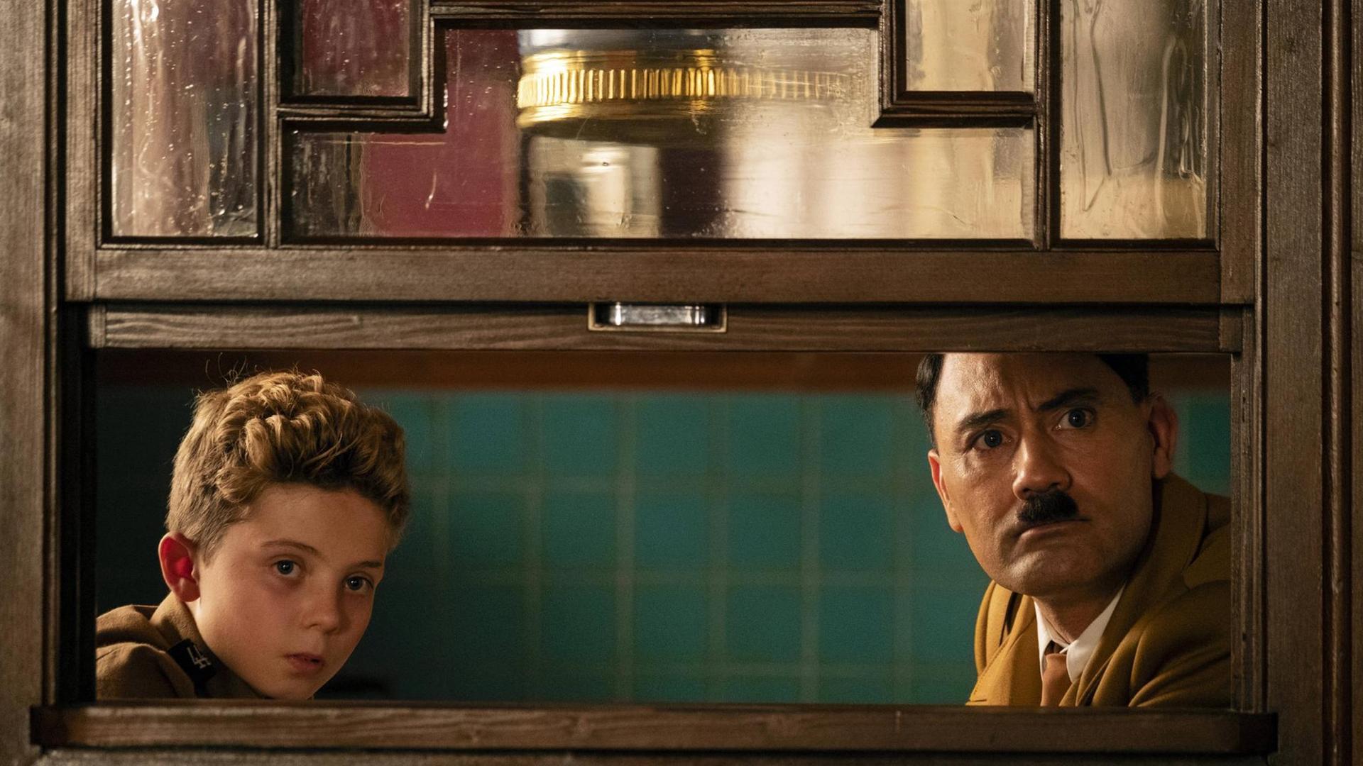 Roman Griffin Davis als Jojo Betzler und Taika Waititi als Adolf Hitler sehen erstaunt in die Kamera Roman Griffin Davis als Jojo Betzler und Taika Waititi als Adolf Hitler sehen erstaunt in die Kamera