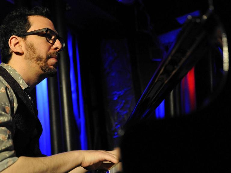 Pianist Omer Klein sitzt auf einer blau-rot ausgeleuchten Bühne am Flügel und spielt.