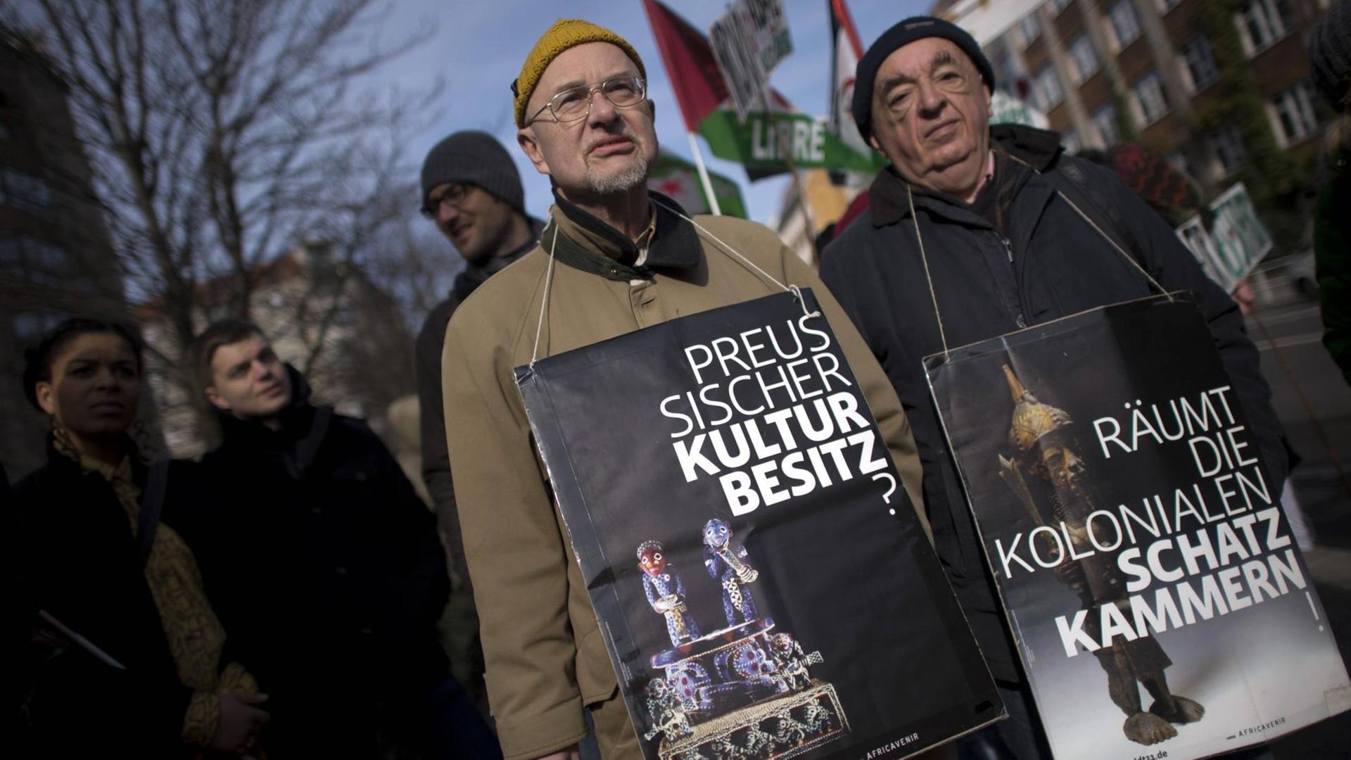 Demonstranten auf dem Gedenkmarsch zur deutschen Kolonialgeschichte mit Plakaten um den Hals, wo der Preussische Kulturbesitz hinterfragt wird und aufgefordert wird, die kolonialen Schatzkammern zu räumen. Demonstranten auf dem Gedenkmarsch zur deutschen Kolonialgeschichte mit Plakaten um den Hals, wo der Preussische Kulturbesitz hinterfragt wird und aufgefordert wird, die kolonialen Schatzkammern zu räumen.