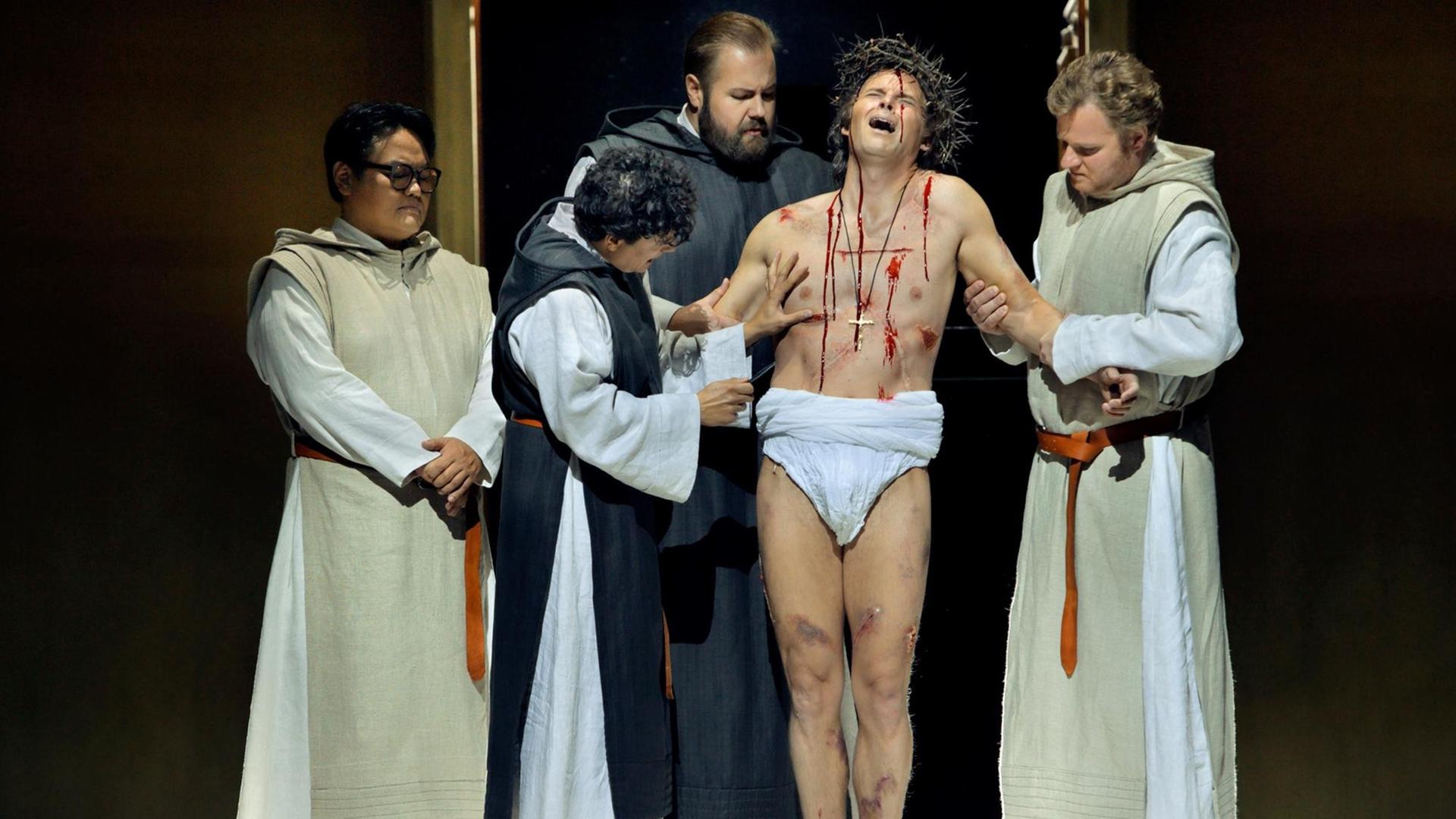 Eine Gruppe von Männern auf einer Theaterbühne stehen um einen aus einzelnen Wunden blutenden Mann herum. Die Operlamm-Szene. Eine Gruppe von Männern auf einer Theaterbühne stehen um einen aus einzelnen Wunden blutenden Mann herum. Die Operlamm-Szene.