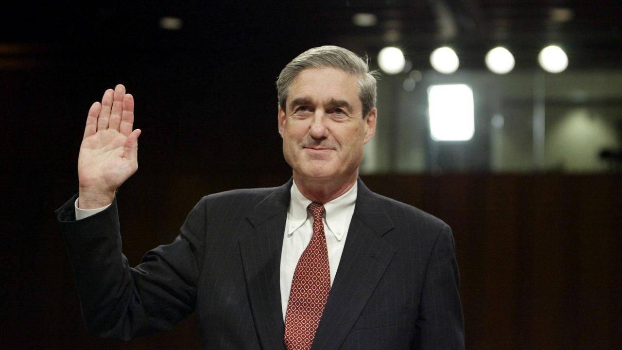 Mueller hebt vor einem dunklen Hintergrund die Hand zum Schwur. 