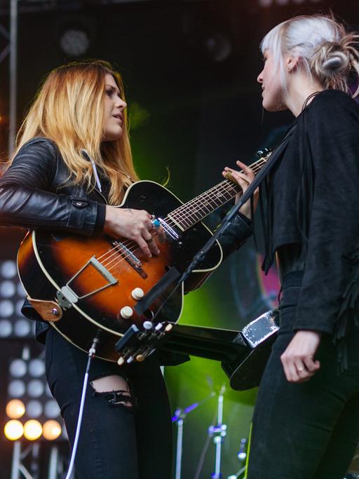 Zwei Frauen mit Gitarren stehen sich auf einer Konzertbühne gegenüber.