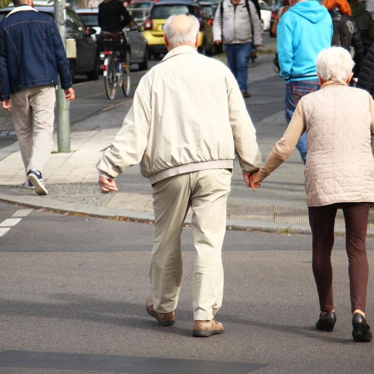 Ein Rentnerpaar überquert eine Straße.