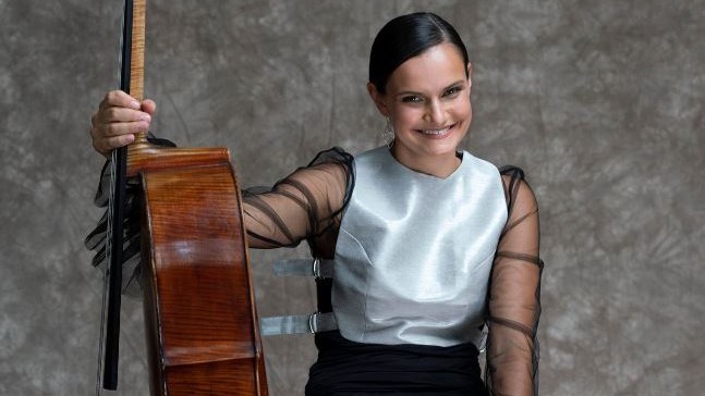 Die Cellistin lacht in die Kamera und hält das Cello mit ausgestrecktem Arm. Die Cellistin lacht in die Kamera und hält das Cello mit ausgestrecktem Arm.