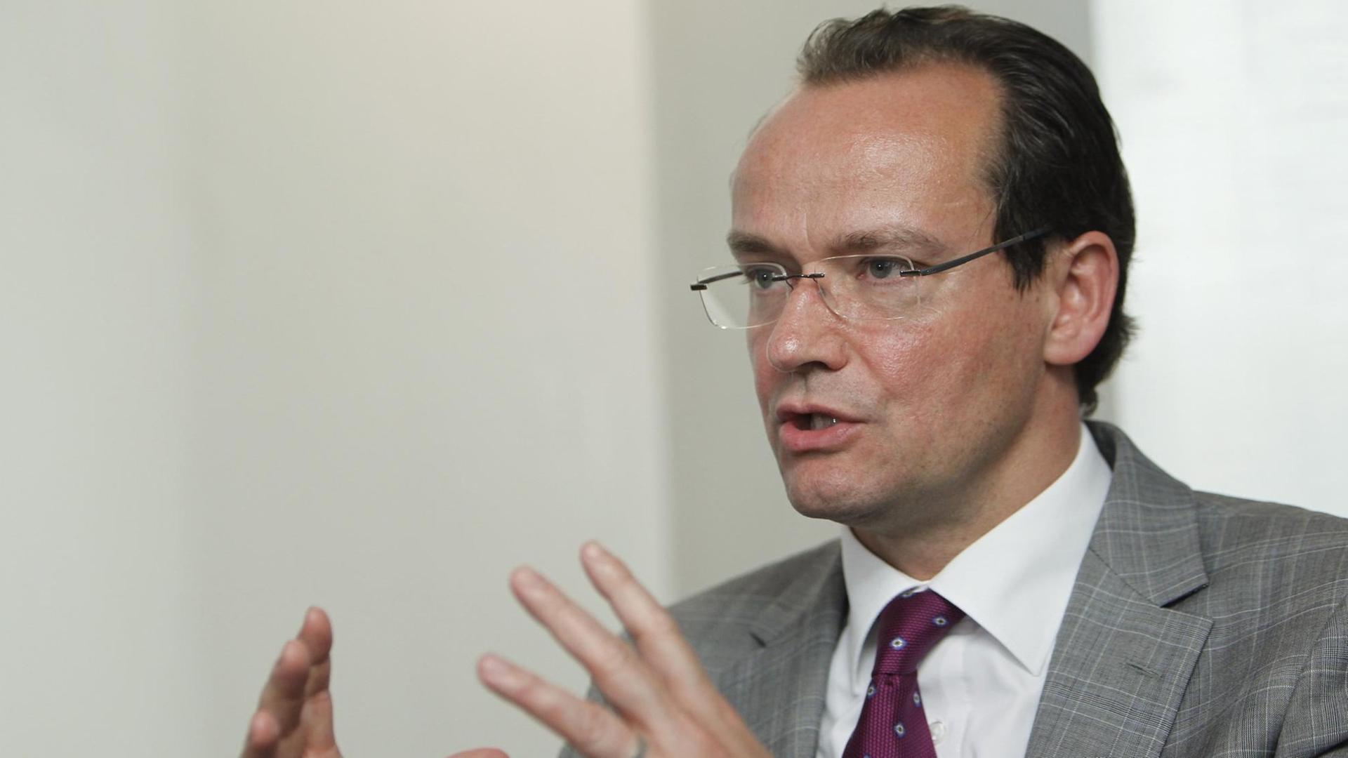 Krichbaum spricht und gestikuliert mit beiden Händen vor einer weißen Wand. Krichbaum spricht und gestikuliert mit beiden Händen vor einer weißen Wand.