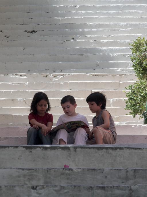 Nauplia, Griechenland: Drei Kinder sitzen mit einer Zeitschrift auf den Stufen einer großen Treppe.