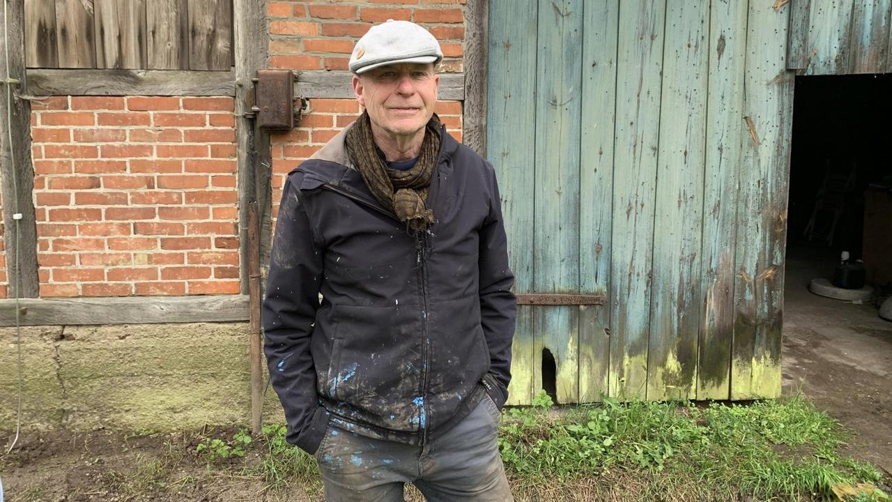 Ein älterer Mann mit Schiebermütze steht vor einer Scheune. Ein älterer Mann mit Schiebermütze steht vor einer Scheune.