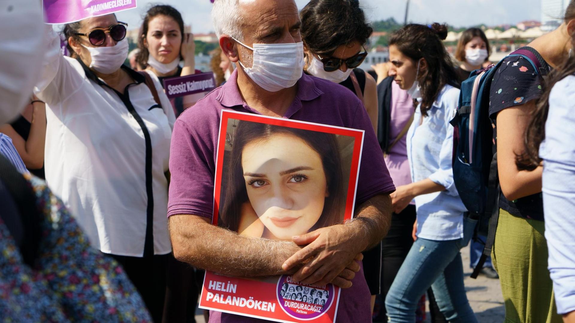 Der Vater der jungen Helin Palandöken hält auf eine Kundgebung ein vergrößertes Foto von ihr in den Händen und trägt dabei Mundschutz.