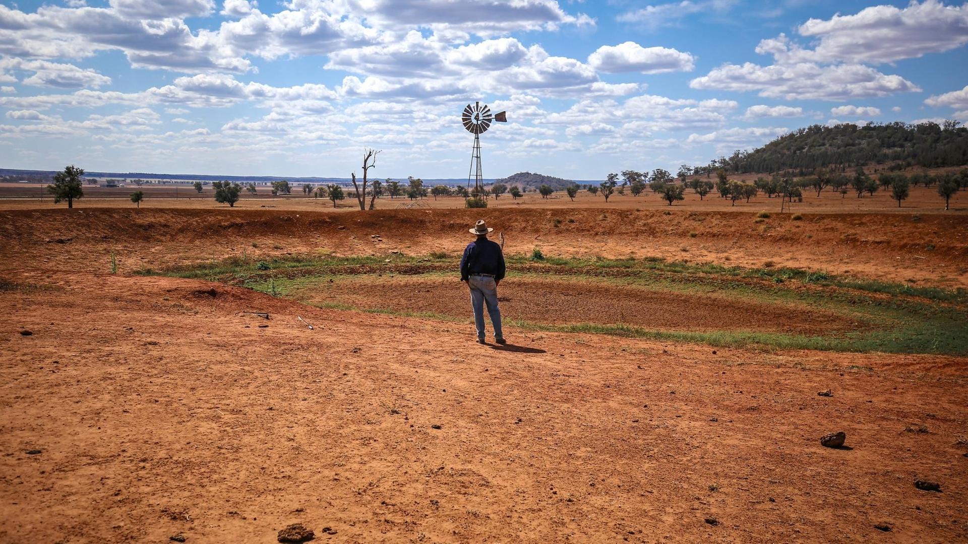 Ein australischer Bauer blickt auf ein Windrad, das einsam in der ausgedörrten Landschaft steht. Ein australischer Bauer blickt auf ein Windrad, das einsam in der ausgedörrten Landschaft steht.
