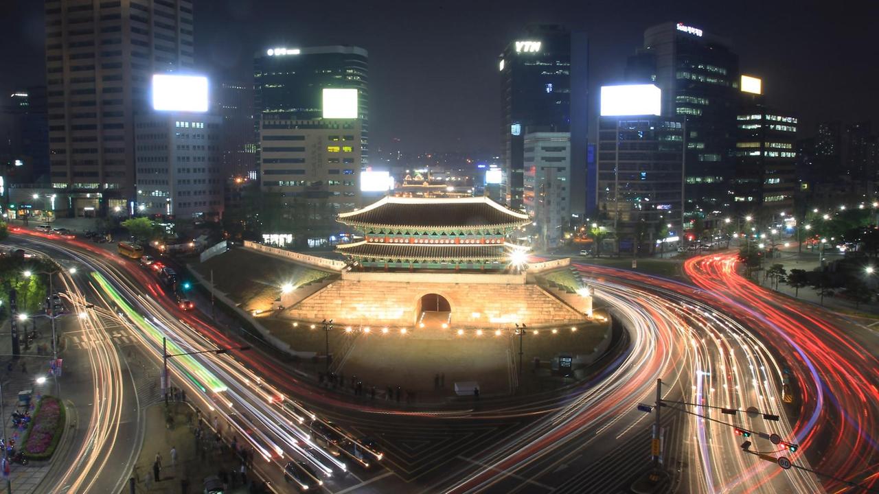 Eine Nachtaufnahme zeigt die illuminierte Innenstadt von Seoul mit Ihren Hochhäusern udn Schnellstraßen. In der Mitte das historische Sungnyemun-Tor.