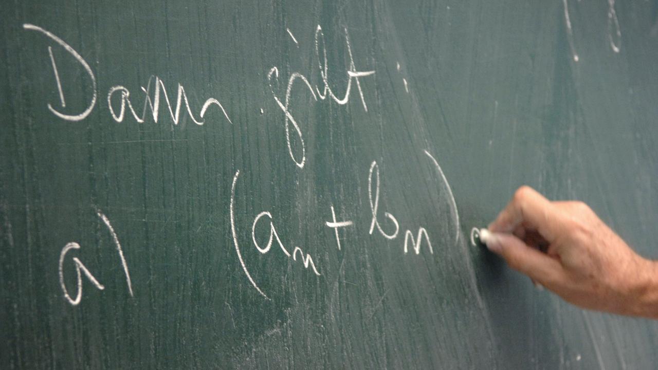 Jemand schreibt eine mathematische Formel auf eine Tafel Jemand schreibt eine mathematische Formel auf eine Tafel