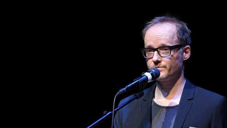 Der Indie-Pop-Musiker und Autor Peter Licht bei einer Lesung mit einem Buch in der Hand. Der Indie-Pop-Musiker und Autor Peter Licht bei einer Lesung mit einem Buch in der Hand.