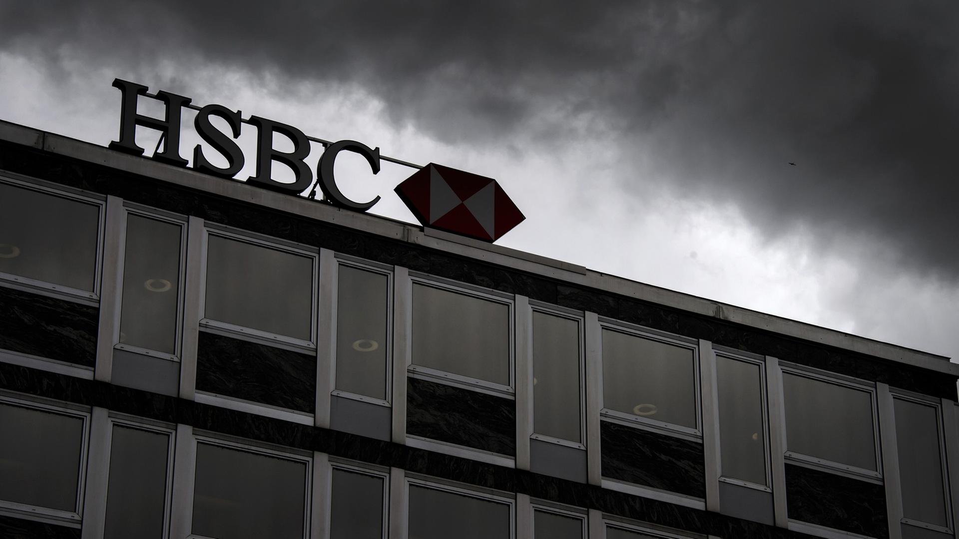 Schriftzug HSBC auf einem Gebäude, über dem dunkle Wolken aufziehen.