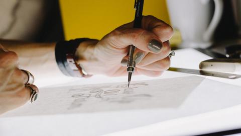 Eine Hand skizziert mit einem ganz feinen Stift etwas auf einem Papier.