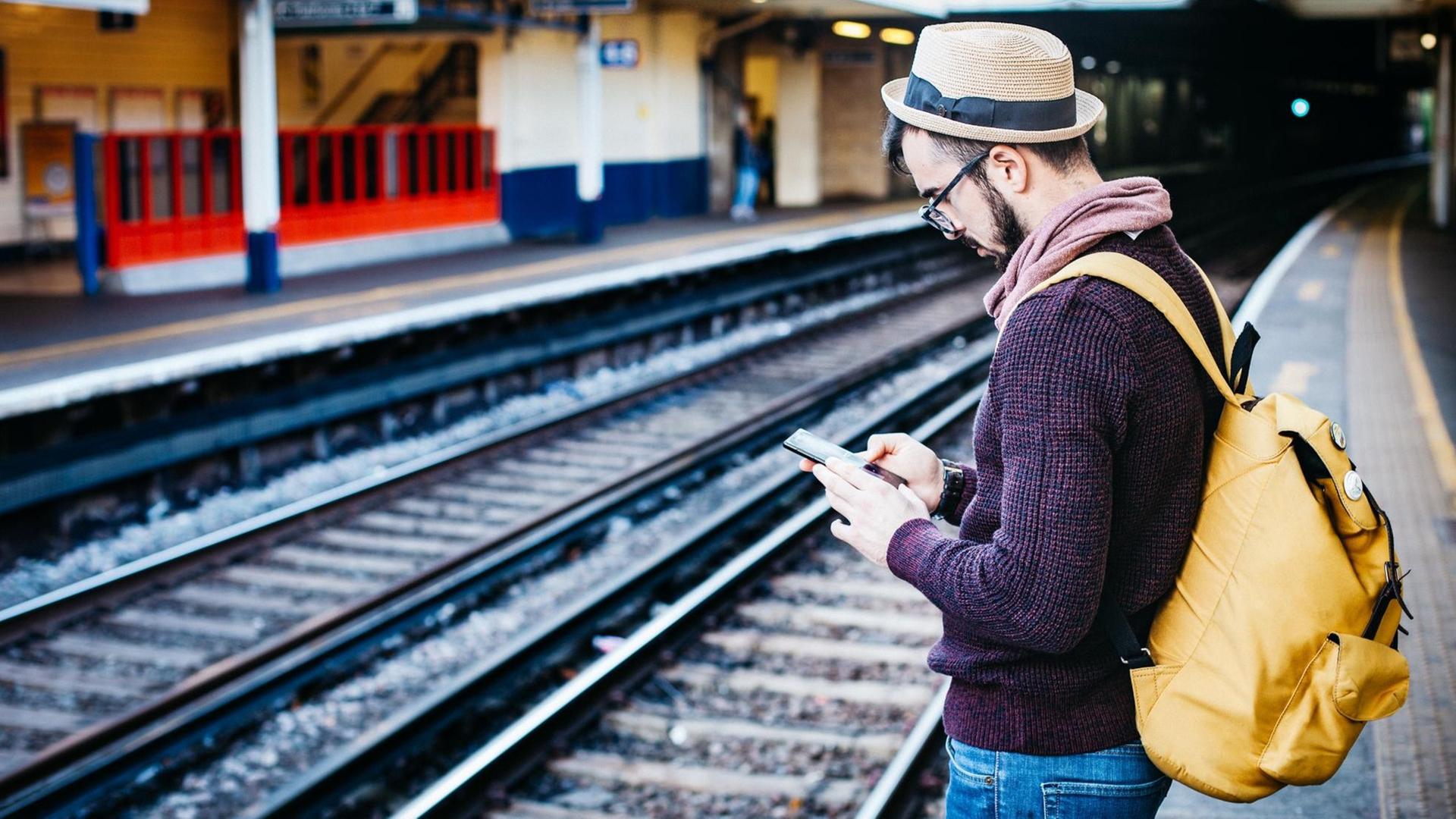 Ein junger Mann steht auf einem Bahnsteig und liest auf seinem Smartphone Ein junger Mann steht auf einem Bahnsteig und liest auf seinem Smartphone
