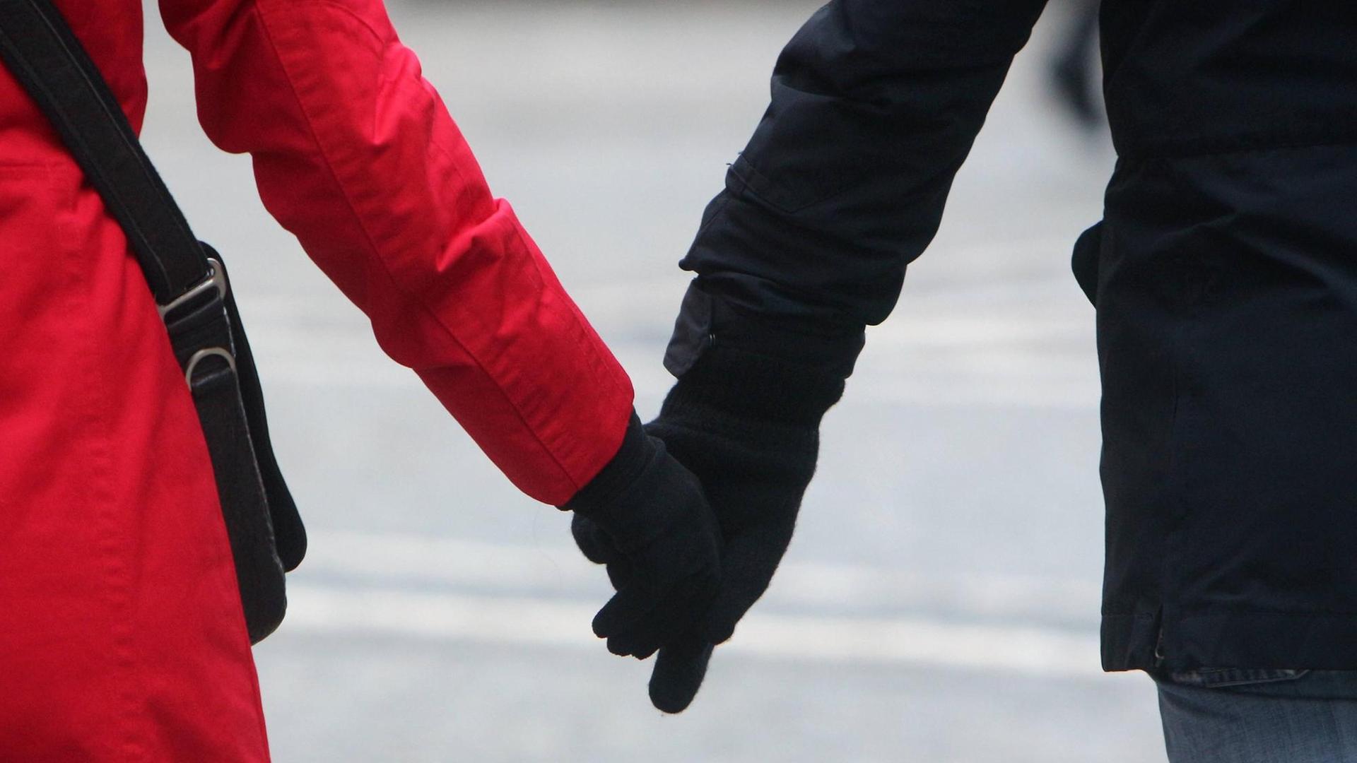 Hand in Hand gehen eine Frau im roten Mantel und ein Mann in schwarzer Jacke über die Straße.