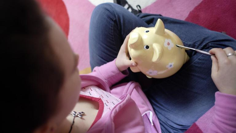Eine Jugendliche plündert ihr Sparschwein mit einem Messer (Symbolbild)