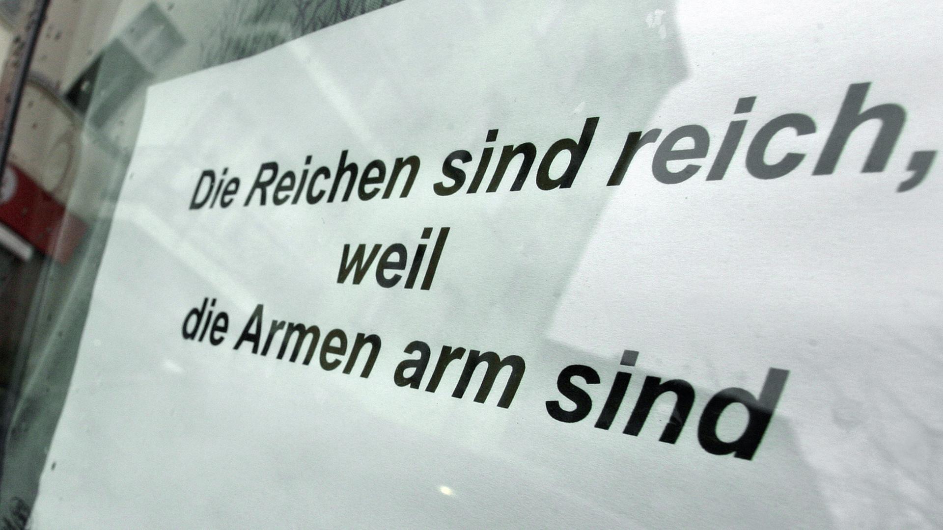 In der Seitenscheibe eines Autos klebt von innen ein Blatt Papier mit der Aufschrift "Die Reichen sind reich, weil die Armen arm sind". In der Seitenscheibe eines Autos klebt von innen ein Blatt Papier mit der Aufschrift "Die Reichen sind reich, weil die Armen arm sind".